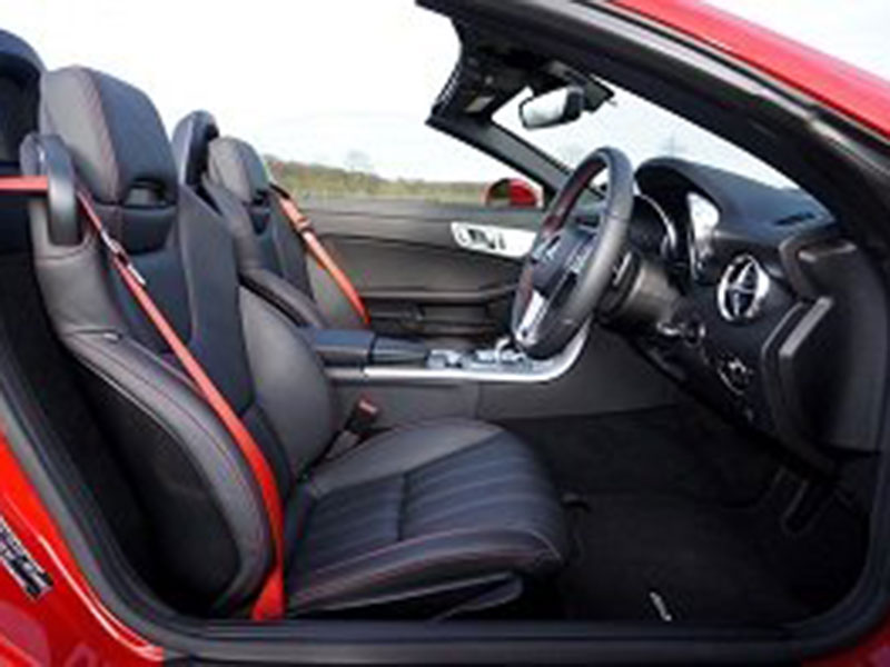 Red convertible car interior, featuring black leather seats with red seatbelt