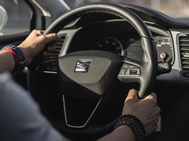 Hands firmly grip a car's black steering wheel