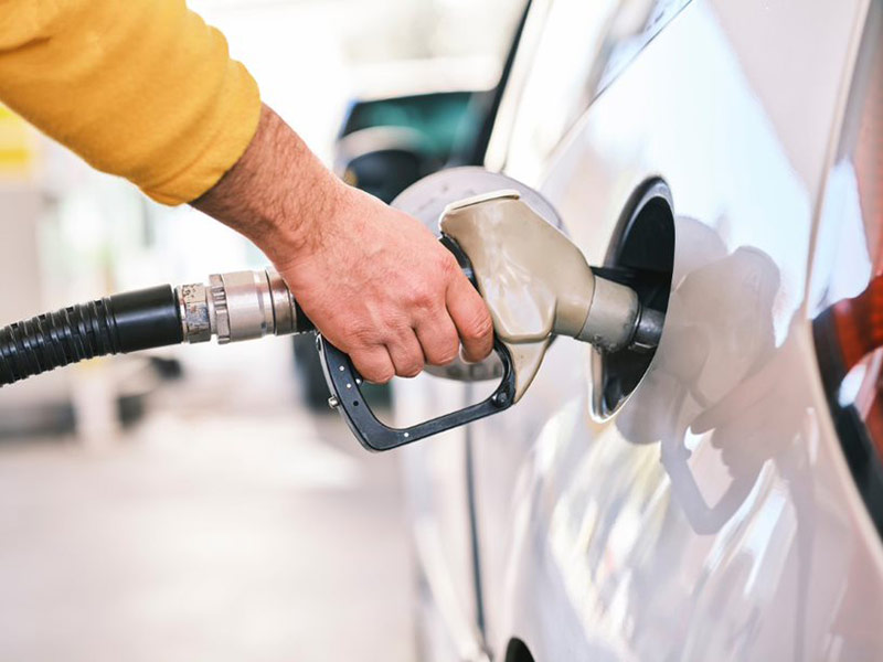 A person in a yellow sweater refuels a car at a gas station